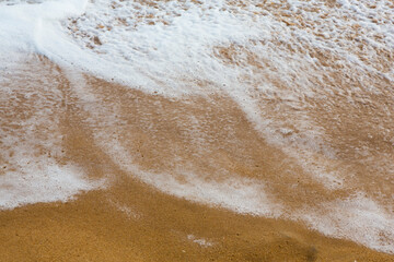 beautiful filled frame close up seascape wallpaper background shot of golden orange sand with white foamy waves of the Indian ocean forming pretty textures and patterns. Pitiwella beach, Sri Lanka