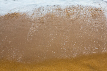 beautiful filled frame close up seascape wallpaper background shot of golden orange sand with white foamy waves of the Indian ocean forming pretty textures and patterns. Pitiwella beach, Sri Lanka