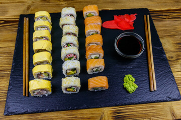 Set of sushi rolls on a black stone slate on wooden table