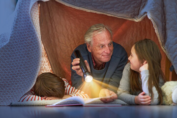 Grandpa reads grandchildren story in tent at home