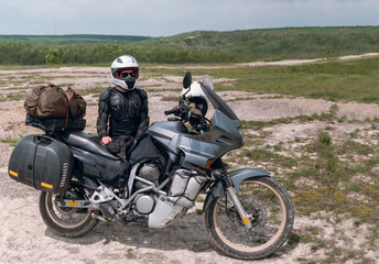 Girl motorcyclist in a helmet. Dressed in a jacket with a turtle, body armor, knee pads. Traveling is an extreme hobby. Safety and body protection. Bike with bags. Copy space panorama.
