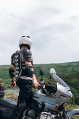 Biker in a helmet and motorcycle equipment, jacket turtle, body armor. Close. In the background a touristic motorcycle. The concept of extreme and hobby. Traveling by bike. vertical photo