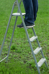 Male feet standing on metal ladder step in garden on green grass lawn. Man working in the garden....