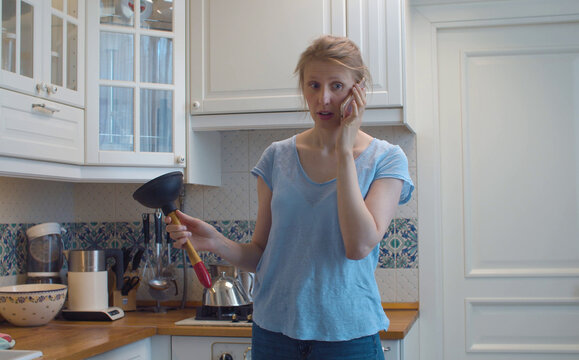 Confused Woman In The Kitchen With A Plunger In Her Hands