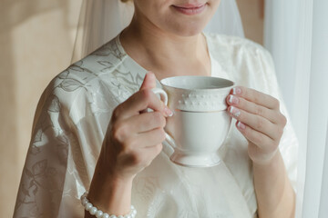 the bride is drinking coffee, bride in a bathrobe drinks tea, morning of the bride, wedding day, bride in a white coat