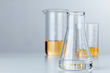 Laboratory glassware with yellow oily liquid on grey background