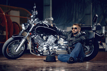 Cool man biker in sunglasses sitting near his motocycle