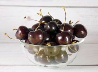 Bowl of ripe cherries on a wooden light background