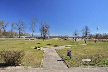Meadow, lawn and trees on a cloudless day, with a bridge in the background.