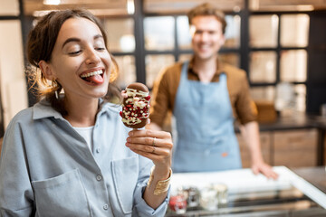 Young and joyful woman with a yummy chocolate ice cream at the shop with seller on the background