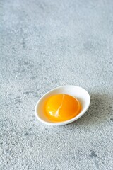 Egg yolk in a white bowl on a gray background. Egg. Product for cooking.