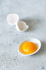 Egg yolk in a white bowl with a shell on a gray background. Egg. Product for cooking.