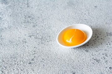 Egg yolk in a white bowl on a gray background. Egg. Product for cooking.