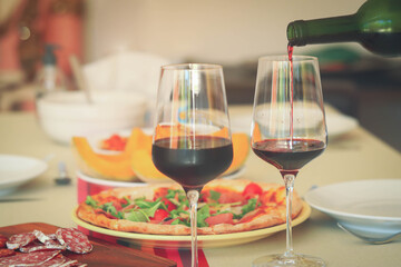 Pouring red wine from bottle into  glasses on table with food background