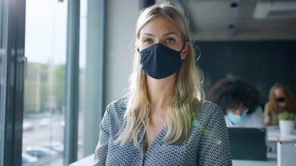 Young woman back at work in office after lockdown, taking off face mask. - Powered by Adobe