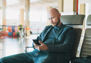Handsome bald bearded man businessman in suit using mobile phone at the airport lounge