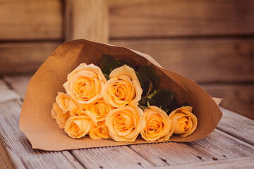 A bouquet of beautiful peach-coloured roses wrapped in brown paper on a wooden bench