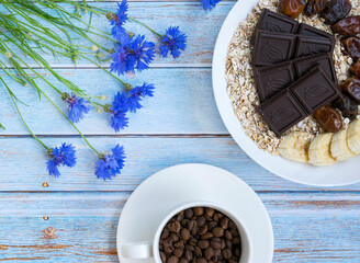 Oatmeal with banana slices, dates. Coffee beans in a mug. Cornflowers. View from above. Ingredients for a healthy diet. Hipster breakfast.