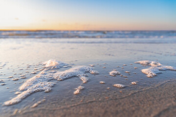 sea foam on the shore, sunset on the background, blurry background