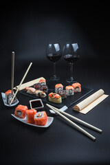 Set of traditional Japanese cuisine on a dark background. Sushi rolls with red wine in a high glass. Asian food frame. Dinner party.