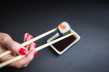A woman holds sushi with chopsticks. sushi roll and soy sauce.