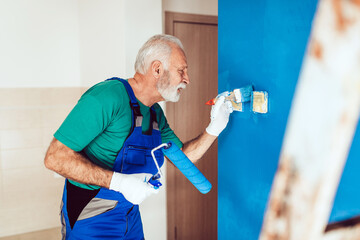 Senior male painter painting a wall. Close up shot on wall painting tools.
