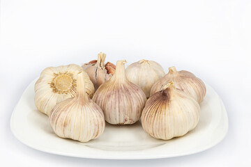 Obraz premium Seven heads of young garlic on a white plate. Close-up. White background.