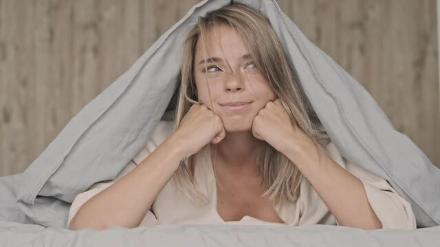 Joyful attractive blonde woman having fun and showing grimaces while lying on bed at home