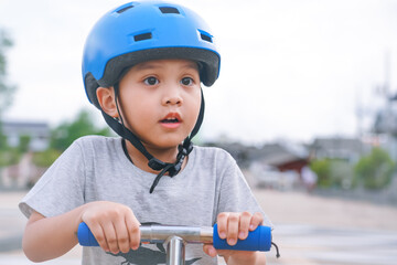 portrait of a young little asian boy wearing sport helmet and holding handlebars of kid scooter 