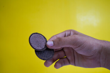hands holding chocolate biscuits on a yellow background with copy space