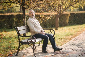 Old gray-haired man rest on the bench in autumn park