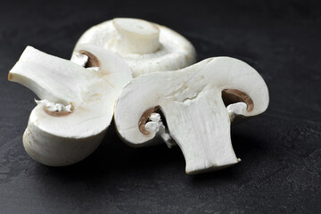 Cutted champignon mushrooms on black background. Vegan food concept.