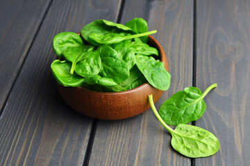 Spinach leaves in wooden bowl over wooden table background. Vegan food trend. Green living concept.