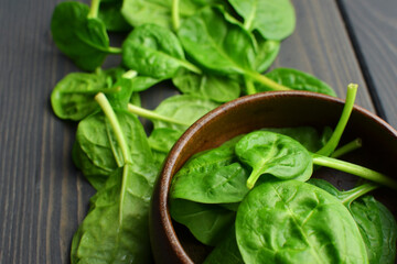Fresh spinach leaves in wooden bowl over old wooden table. Healthy vegan food. Green living and eco-conscious concept.