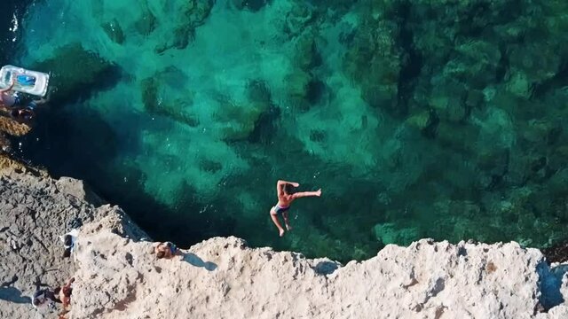 Slow motion aerial top down shot of man jumping from a cliff into clear turquoise water in Mallorca, Spain - Balearic Island Holiday