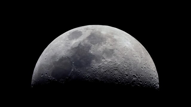 The Telescope Zooming On The Moon stock video shows First Quarter moon over a dark black sky, as seen from the POV of a spaceship flying towards the moon.