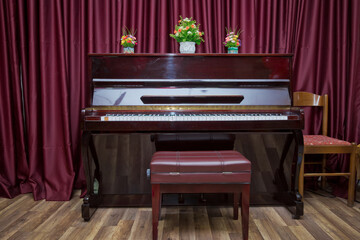 Old wooden piano keys on wooden musical instrument in front view . modern red piano bench . Big brown wooden piano and red bench close up in room .