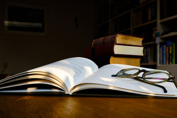 Close up of open text book with eye glasses on wooden desk in library. Old books and bookshelf background. Education concept. Selective focus