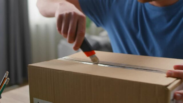 Close up shot as a young man opens a parcel with a knife