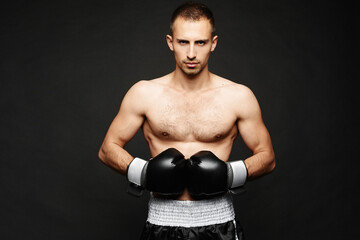 Fototapeta na wymiar A young male boxer with athletic perfect body in boxing gloves isolated at dark background