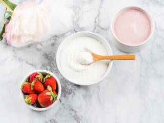Collagen protein powder in bowl with wooden spoon on marble table. Adding collagen supplement to strawberry yogurt. Healthy breakfast, flat lay