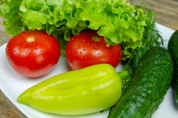 Fresh juicy vegetables peppers, tomatoes, cucumbers lettuce leaves with water drops beautifully laid out on a white plate close-up. Vegetables are in the form of a funny face