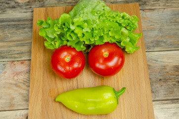 Fresh juicy vegetables peppers, tomatoes, cucumbers lettuce leaves with water drops are beautifully laid out on a wooden Board close-up. Vegetables are in the form of a funny face, top view