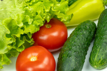 beautiful fresh, juicy vegetables on a white plate: fresh peppers, tomatoes, cucumbers, lettuce, dill