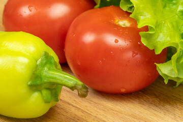 Beautiful, juicy vegetables with water drops Peppers, tomatoes, lettuce leaves on a wooden Board close-up