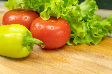 Beautiful, juicy vegetables with water drops Peppers, tomatoes, lettuce leaves on a wooden Board close-up