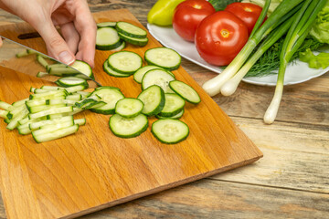 women's hands with a knife cut a cucumber on a cutting Board, next to a plate of vegetables