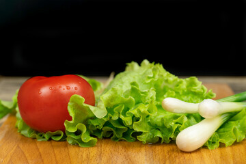 green lettuce leaves, tomato, green onion with water drops on a wooden Board, black background in the background, copy space