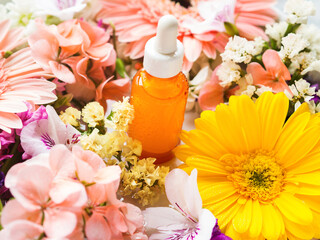 Skin care serum in orange bottle with dropper with beautiful flowers around. Natural beauty product