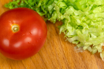 Sliced lettuce leaves and a whole ripe tomato on a wooden Board close up, top view, copy space